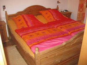 Cama de madera con sábanas y almohadas de color naranja y rojo en Ferienhaus Sachrang en Sachrang