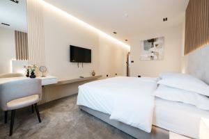 a white bedroom with a bed and a desk and a tv at Hotel Kod Barića in Grude