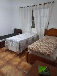 a bedroom with two beds and a window with curtains at Aconchego in Guarujá