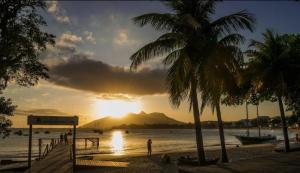 a sunset on a beach with palm trees and the ocean at POUSADA AMAZONAS in Rio das Ostras +12 photos