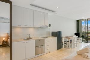 a kitchen with white cabinets and a table with chairs at 126 Santai - Ground Floor Studio Apartment by uHoliday in Casuarina