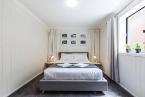 Fernberg Cottage - Sunny Queenslander Charm في بريزبين: غرفة نوم بيضاء بسرير ومصباحين
