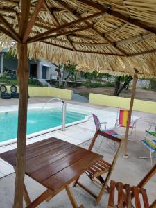a table and a chair under a straw umbrella next to a swimming pool at Pousada Chacara Cururu in Alter do Chao