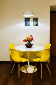 a table with yellow chairs and a vase of flowers at Apto com VISTA do Pão de Açúcar, VARANDA, PISCINA, SAUNA, ACADEMIA, COZINHA COMPLETA, GARAGEM, PORTARIA 24h e MINI MERCADO in Niterói