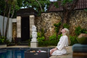 a woman sitting next to a swimming pool at The Club Villas Seminyak in Seminyak