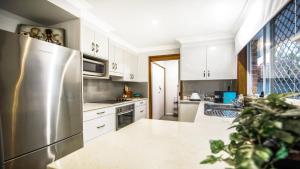 La cuisine est équipée de placards blancs et d'un réfrigérateur en acier inoxydable. dans l'établissement Shore Fun - Ettalong Beach, à Ettalong Beach
