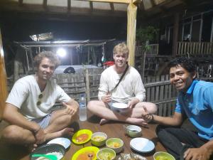 three men sitting around a table with bowls of food at GoodMuning SurfCamp in Taliwang