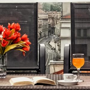 City Boutique Hotel في سراييفو: طاولة مع كتاب و مزهرية من زهور الأقحوان الحمراء و شراب