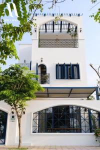 ein weißes Haus mit schwarzen Fenstern und einem Baum in der Unterkunft Apple Hause Venuestay in Phan Rang