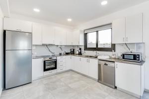 una cocina con armarios blancos y electrodomésticos de acero inoxidable en Villa Elpida THREE by Ezoria Villas in Timi, Paphos en Pafos