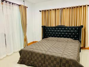 a bedroom with a bed with a black headboard and curtains at Ban Sam Bai Thao 