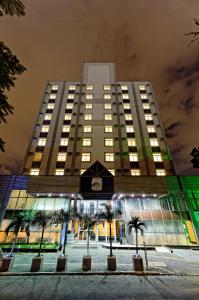 a tall building with palm trees in front of it at Sables Hotel Guarulhos in Guarulhos