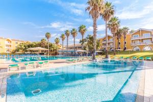 una piscina en un complejo con palmeras y edificios en Vibra Blanc Palace Aparthotel, en Sa Caleta