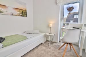 een witte slaapkamer met een bed, een stoel en een raam bij Düünleev in Langeoog