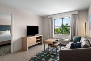 ウェストパームビーチにあるHomewood Suites by Hilton West Palm Beachのソファ、テレビ、ベッドが備わるホテルルームです。