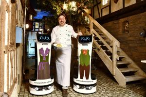 Un uomo è in piedi accanto a due robot da cucina di digitales Event & Hochzeitshotel Zum grünen Baum a Taltitz