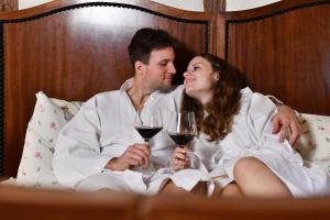 digitales Event & Hochzeitshotel Zum grünen Baum في Taltitz: رجل وامرأة يجلسان في السرير مع أكواب من النبيذ