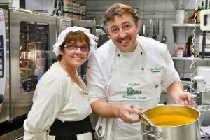 Un uomo e una donna in una cucina con una pentola di zuppa di digitales Event & Hochzeitshotel Zum grünen Baum a Taltitz
