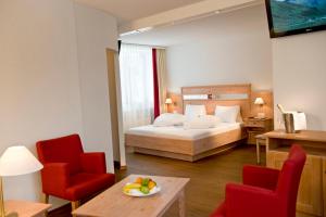 a hotel room with a bed and two red chairs at Quellenhof UNIQUE in Leukerbad