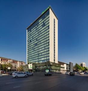 un edificio alto con coches estacionados en un estacionamiento en Holiday Inn - Tbilisi, an IHG Hotel en Tiflis