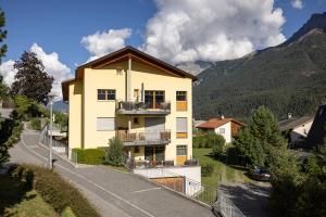 a yellow house with a balcony and mountains in the background at Trü-Sura Nr. 3 in Scuol
