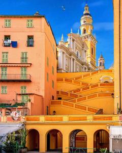a yellow building with stairs and a clock tower at Les Logettes-plage-centre in Menton
