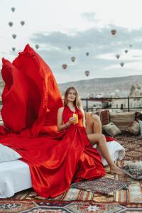 Una donna con un vestito rosso seduta su un letto con un ombrello rosso di Angel View Suites a Göreme