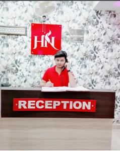 un hombre sentado en una recepción con una señal roja y blanca en Nilansh homes and hotels, en Lucknow