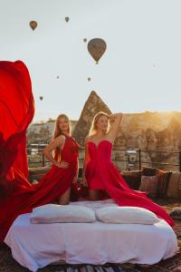 two women in red dresses sitting on a bed with the pyramid at Angel View Suites in Goreme