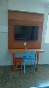 Elle comprend un bureau avec une télévision et une chaise bleue. dans l'établissement Segunda Casa- Seu cantinho na Praia do Morro em Guarapari - Quartos suítes 2 até 4 pessoas, à Guarapari