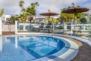 a swimming pool with an umbrella and chairs at Jardines del Sol in Playa Blanca