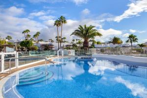 a large swimming pool with palm trees in the background at Jardines del Sol in Playa Blanca