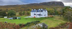 a large white house on a green field with a mountain at Inchnadamph Explorers Lodge in Inchnadamph