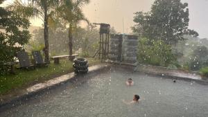 ein Kind, das im Regen im Pool schwimmt in der Unterkunft Monsonkeang Camping view ม่อนสันเกี๋ยง in Mae Chaem