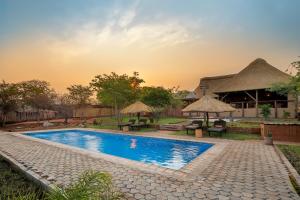 una piscina con mesas y sombrillas junto a un edificio en The Nkhosi Livingstone Lodge and Spa, en Livingstone