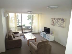 ein Wohnzimmer mit einem Sofa, einem TV und einem Tisch in der Unterkunft Manly Paradise Motel & Apartments in Sydney