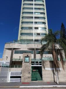 um edifício alto com uma palmeira em frente em Apartamento Cidade Ocian - Praia Grande - Edifício Van Gogh - Alto padrão 94mts - 2 Suítes na Praia Grande