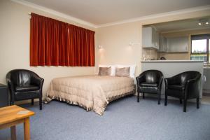 a bedroom with a bed and two chairs at Alpenhorn Motel in Te Anau