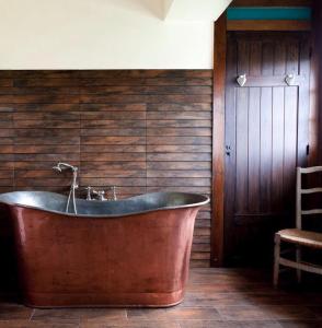 a copper tub in a bathroom with a wooden wall at Chambres d'Hôtes Manoir de Beaumarchais in Les Chapelles-Bourbon