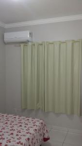 1 dormitorio con cortinas verdes, 1 cama y aire acondicionado en Casa Bombinhas temporada en Bombinhas