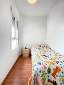 Un dormitorio con una cama con un edredón colorido y una ventana en Apartamento Cerca del Mar y aeropuerto, en Alicante