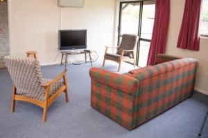 ein Wohnzimmer mit einem Sofa, 2 Stühlen und einem TV in der Unterkunft Alpenhorn Motel in Te Anau