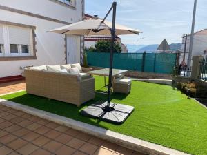 a patio with a couch and an umbrella and grass at Casa de María in Muros