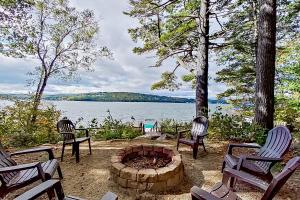 a fire pit with three chairs and a lake at American Dream on Lake Winnipesaukee in Meredith