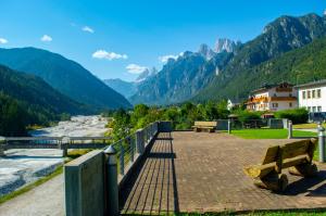 a bridge with benches next to a river and mountains at Albergo Serena in Auronzo di Cadore