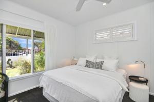 a white bedroom with a bed and a window at Coastal Escape in Long Jetty