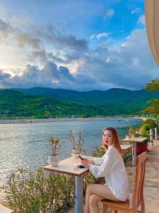 a woman sitting at a table by the water at Chau Gia Hotel in Vĩnh Hy