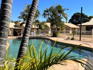 una piscina con palmeras en un patio en Western Heritage Motor Inn, en Moranbah