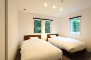 two beds in a room with two windows at Albatross Karuizawa in Karuizawa