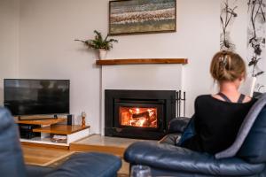 a woman sitting in a chair in front of a fireplace at Driftwood in Coles Bay